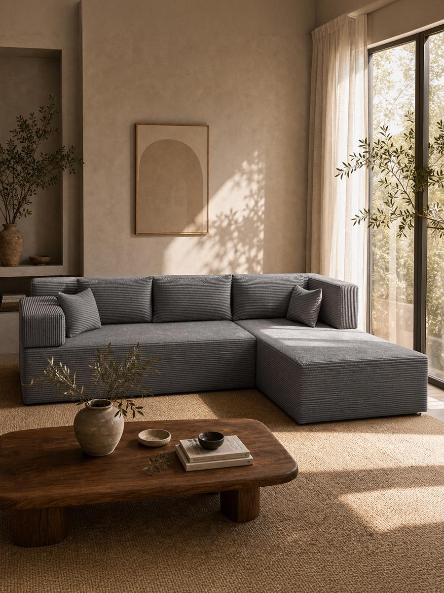 A grey ribbed modular sectional sofa with a chaise end, in a sunlit living room behind a low wooden coffee table